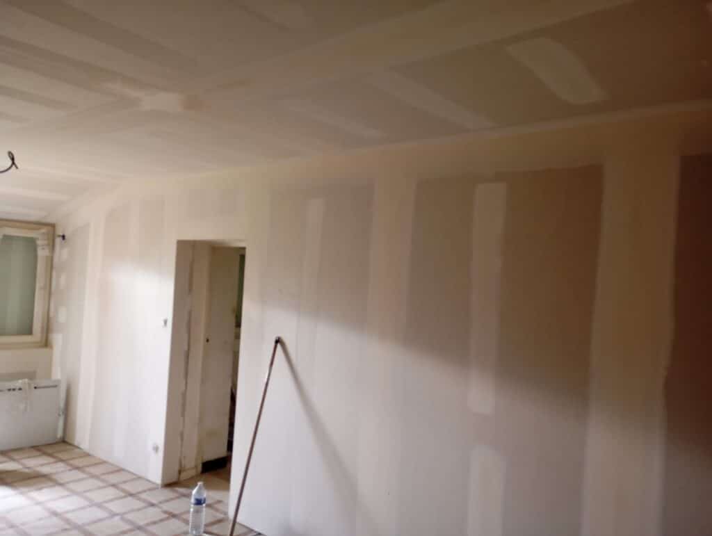 Pièce en cours de rénovation avec plaques de plâtre et joints terminés sur les murs et le plafond.