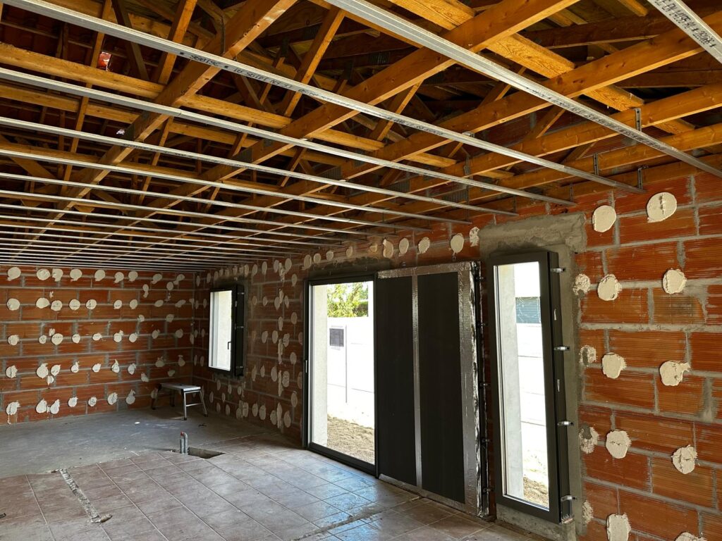 Chantier de rénovation : murs en briques, charpente bois et rails métalliques pour faux plafond suspendu.