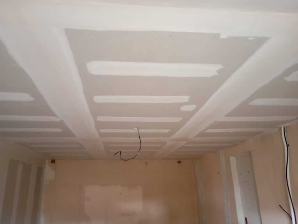 Plafond en plaques de plâtre avec joints enduits et câbles électriques dans une pièce en cours de rénovation.